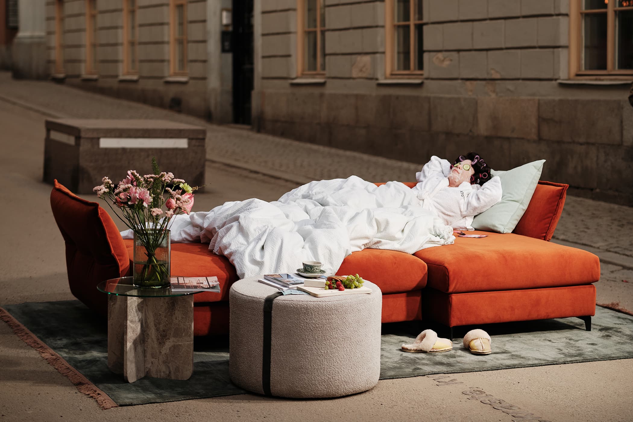 Katten divan bäddsoffa. Salvador, sammet - 14 Rost. Orange bäddsoffa med divan, 270cm bred, med förvaringsutrymme under sitsen och smala, vinklade armstöd i polyestersammet. Stor rund fotpall, 70cm i diameter, i 100% polyester.